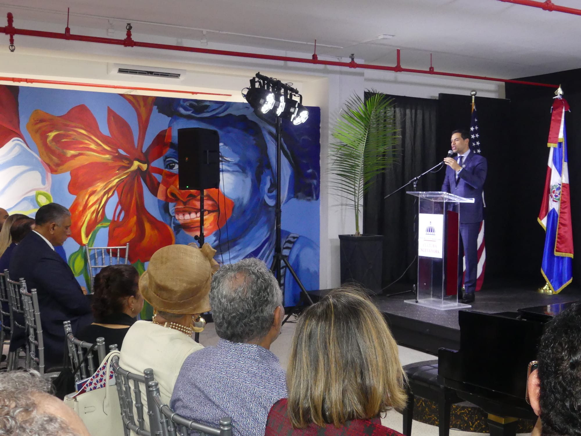 Hombre dando discurso en evento cultural con público.