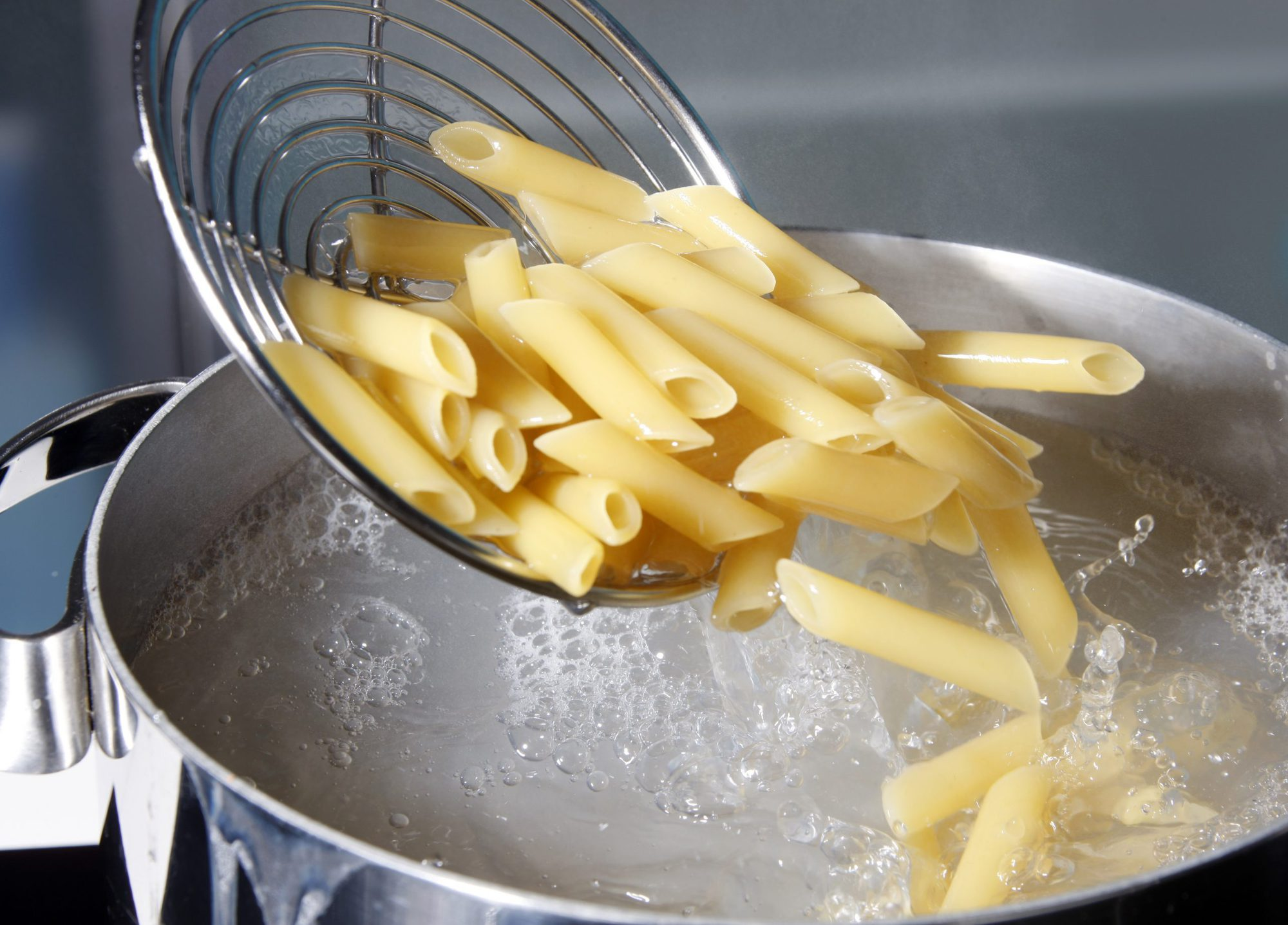 Pasta penne escurriendo agua hirviendo en colador.