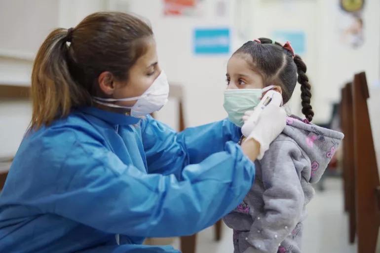 Doctora mide temperatura a niña con mascarilla