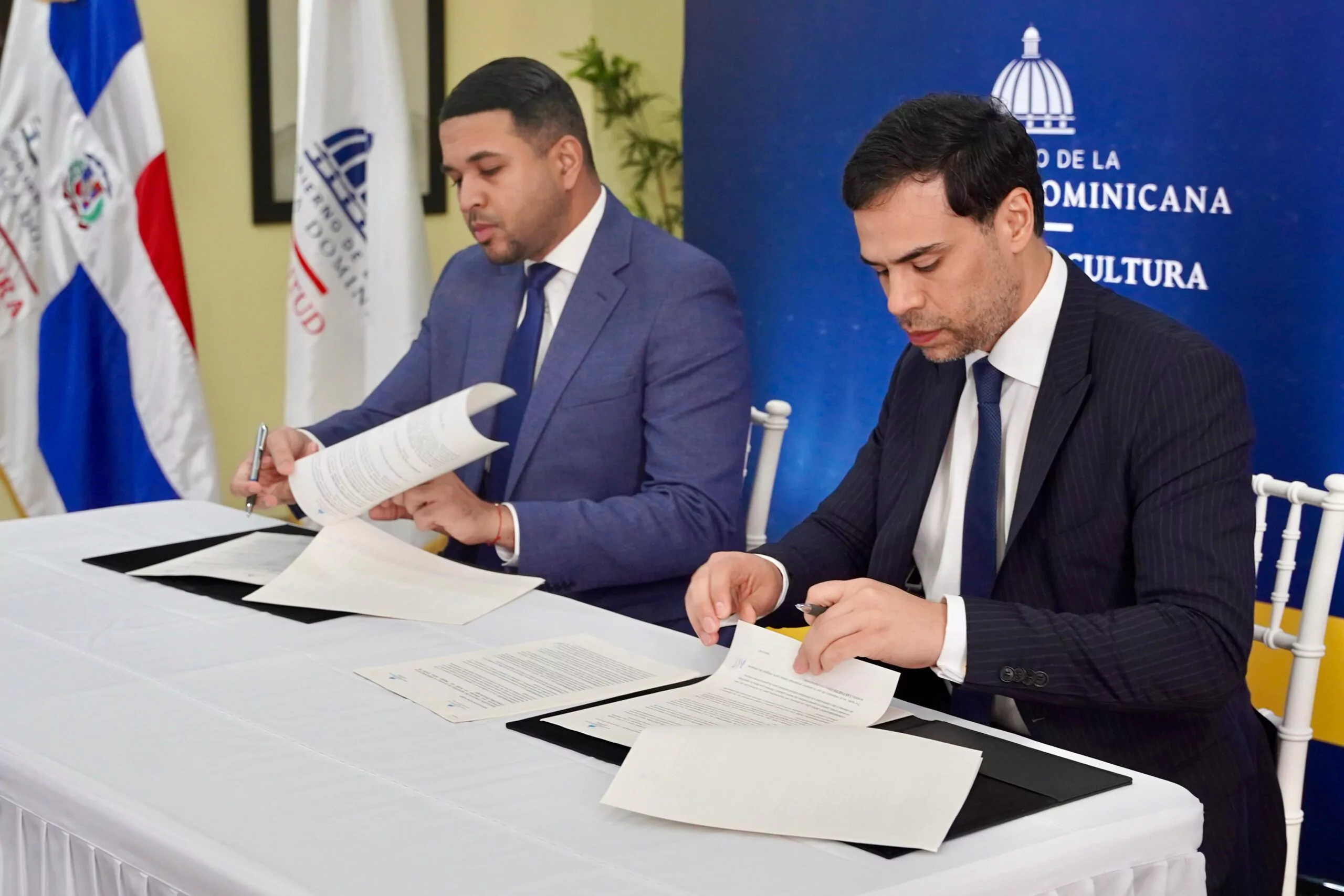 Dos hombres firmando documentos oficiales en oficina.