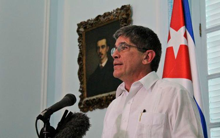 Hombre hablando junto a bandera cubana.